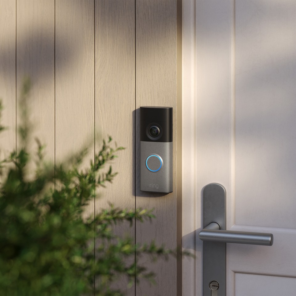 Ring doorbell on a wooden panel next to a white door.