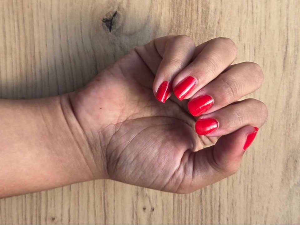 A hand with bright red fingernails resting on a light wooden surface.