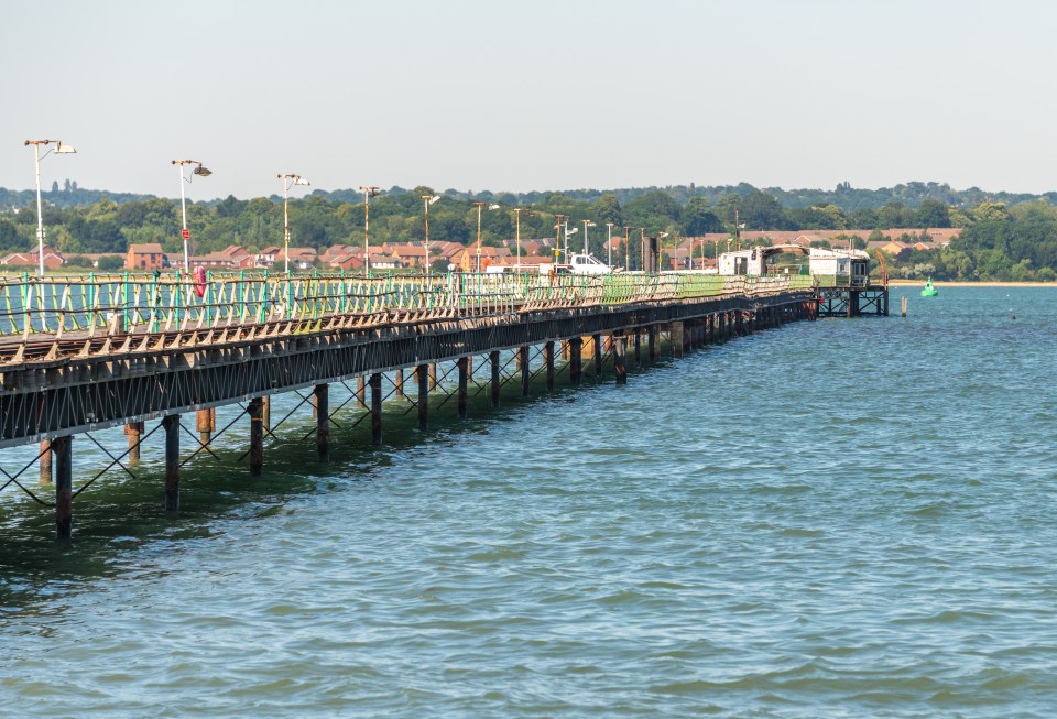 Hythe Pier in Hampshire extending into Southampton Water, with a village and lush trees in the background.