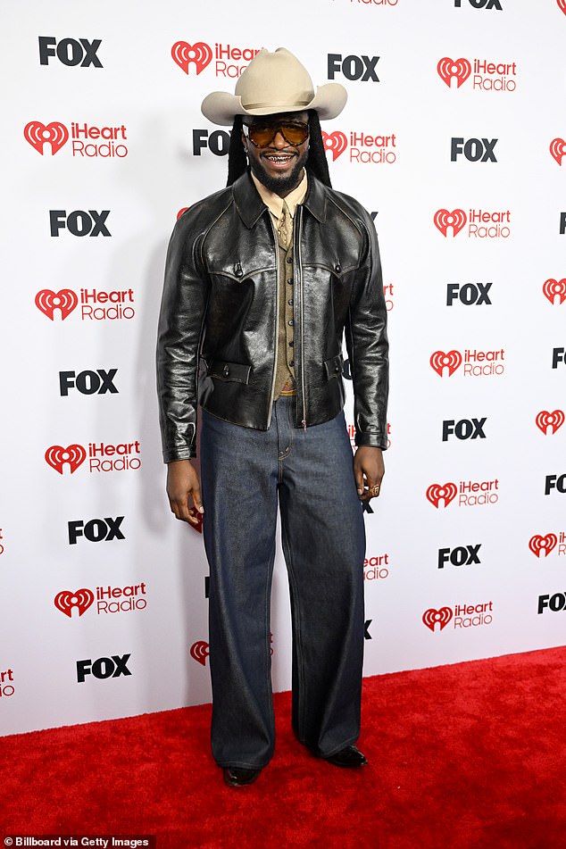 Shaboozey showed off a shiny white gold grill in his mouth, which the country rapper styled with his go-to cowboy hat, a fitted leather jacket and straight-leg jeans