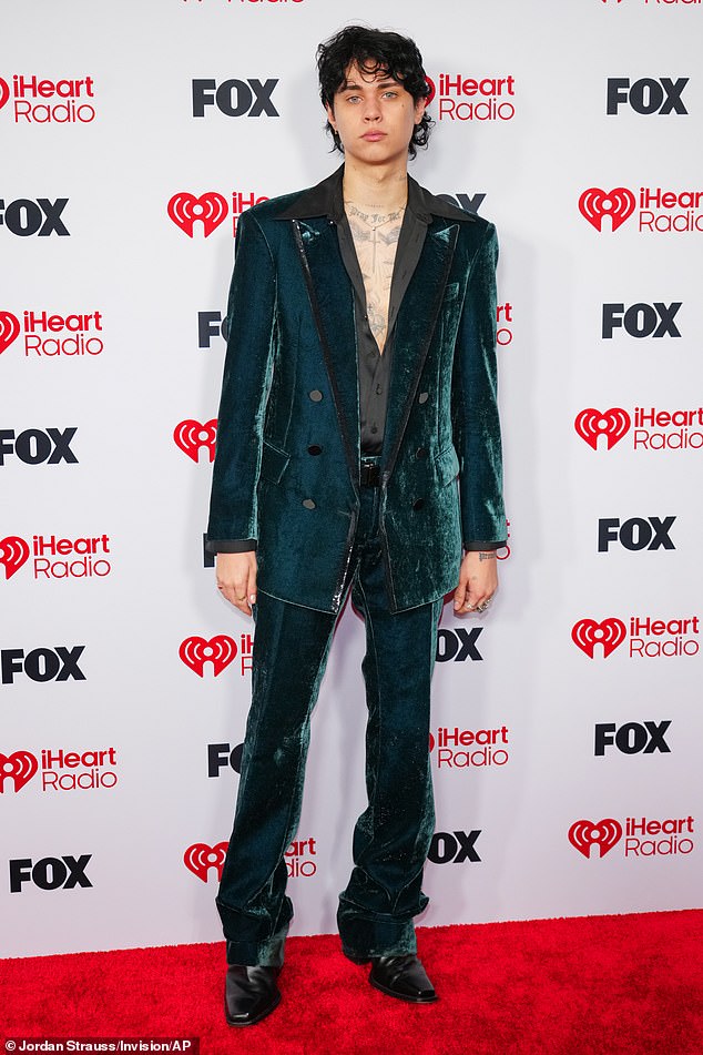 Travis Barker’s nepo baby son Landon Barker, 22, who put his tattooed chest on display by leaving the silky black shirt under his teal velvet jacket unbuttoned