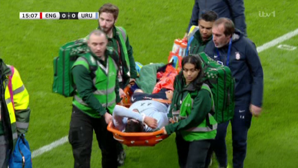 A soccer player is carried off the field on a stretcher by several medical staff members.