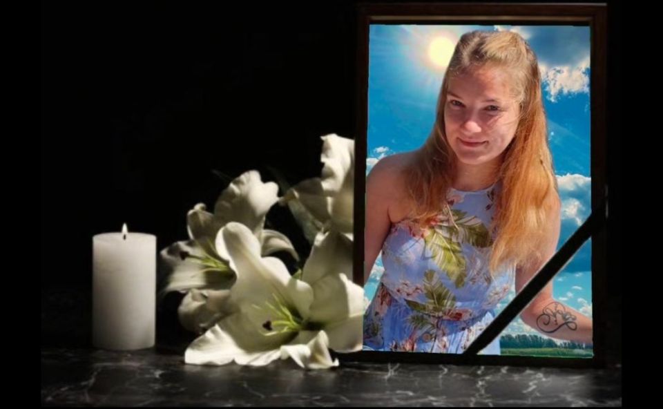 A burning candle, white lilies, and a picture of Orinta Narbutaite, a young woman with long blonde hair, against a blue sky.