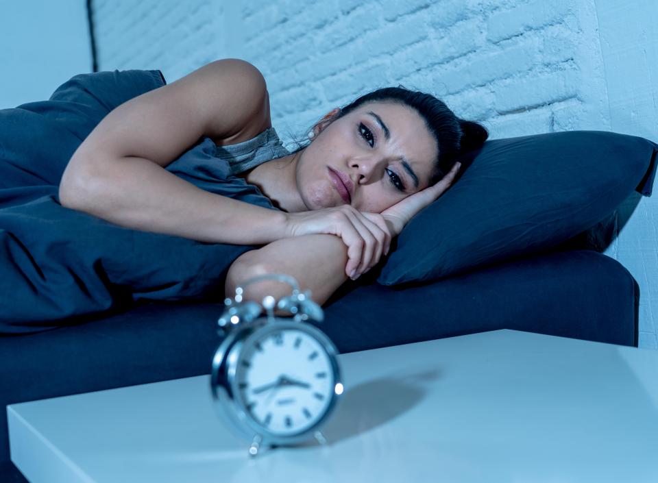 A woman suffering from insomnia lies in bed at night, staring at an alarm clock.