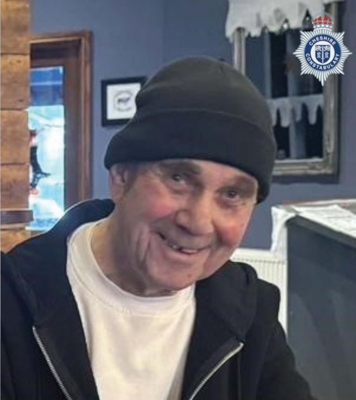 A smiling John McColl wearing a black beanie and black hooded jacket over a white t-shirt.