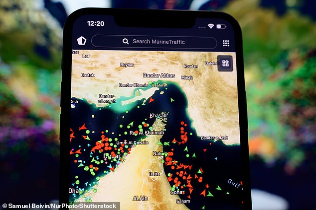 A smartphone screen displaying the MarineTraffic map shows a high concentration of ship beacons in the Strait of Hormuz