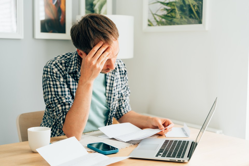 A pensive man reviewing financial documents and using a laptop to manage family finances.