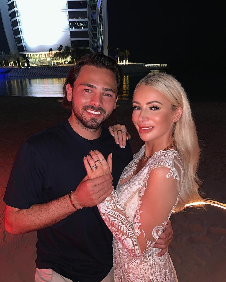 A man and woman pose for a photo on a beach at night in Dubai, with a lit-up hotel in the background.