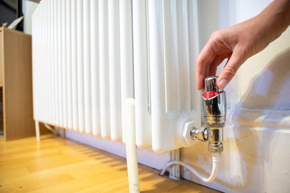 Hand turning a silver radiator valve with red markings on a white radiator.