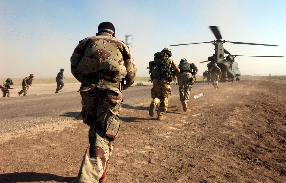 Soldiers in camouflage uniforms running towards a Chinook helicopter in a dusty, desert landscape.