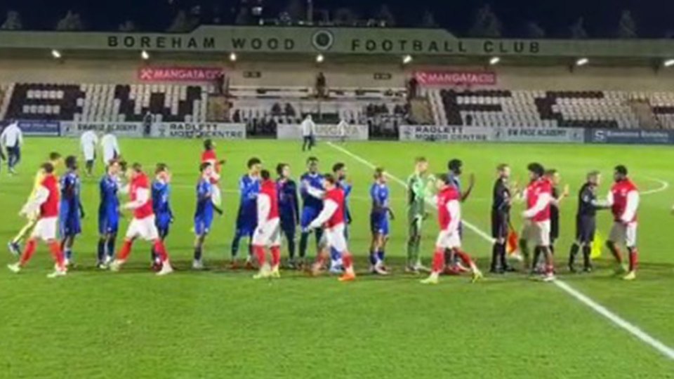 Football players in red and blue jerseys line up to shake hands on a field under stadium lights.