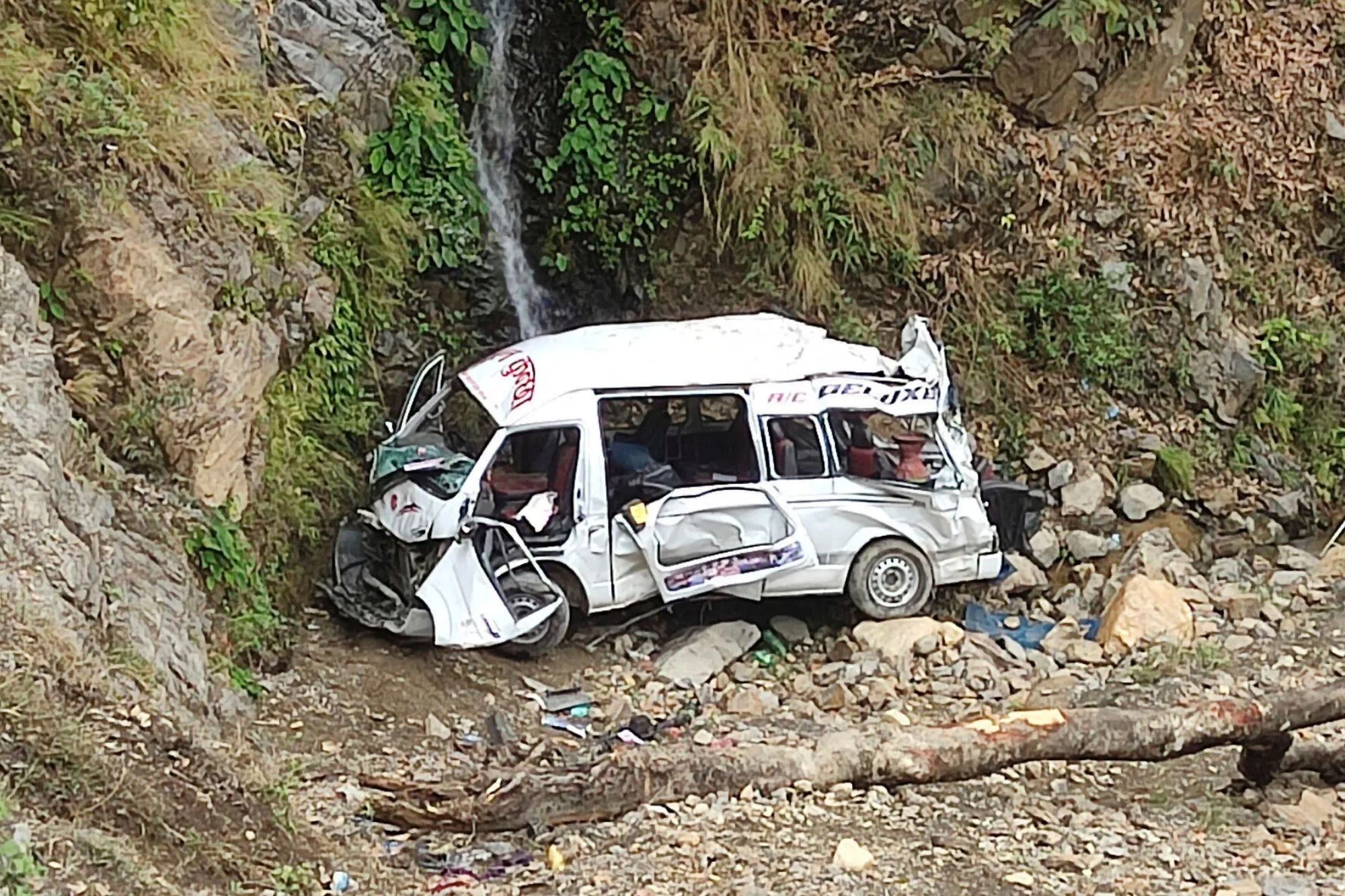 An image collage containing 1 images, Image 1 shows The wreckage of a white bus sits at the bottom of a steep, rocky slope next to a small waterfall
