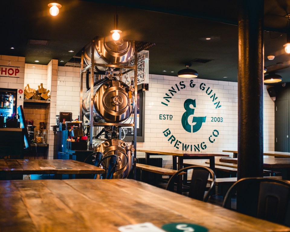 Inside a pub with exposed brewing tanks and "Innis & Gunn Brewing Co" on the wall.