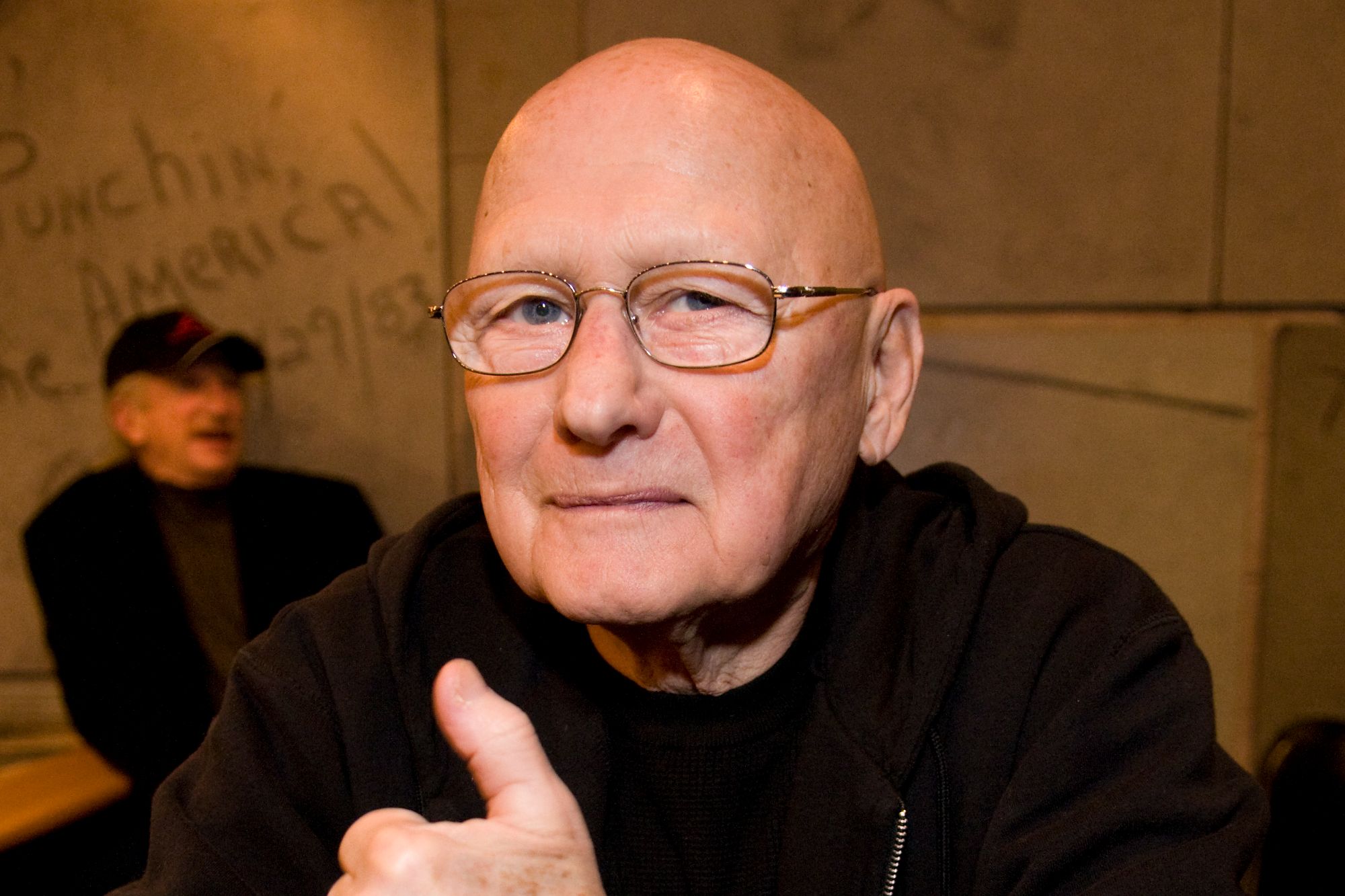 An image collage containing 1 images, Image 1 shows James Tolkan, bald and wearing glasses, gives a thumbs up