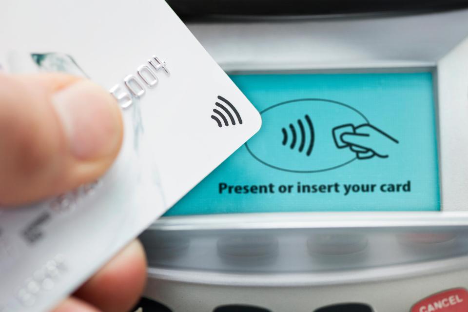 Close-up of a hand holding a credit card over a contactless card machine.