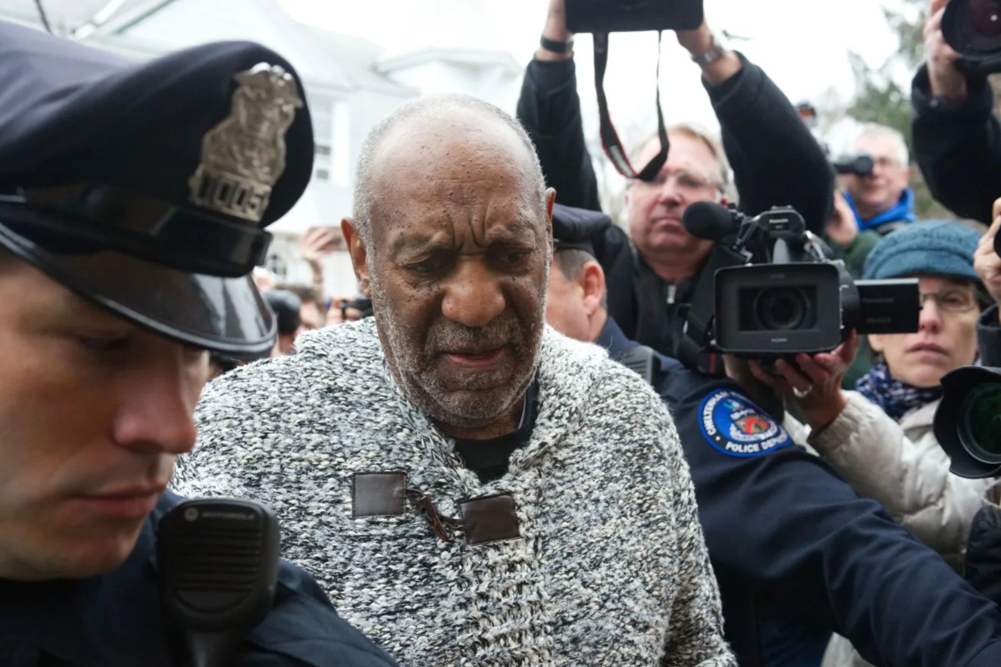 An image collage containing 1 images, Image 1 shows Bill Cosby arriving for his sexual assault trial, surrounded by a police officer and media