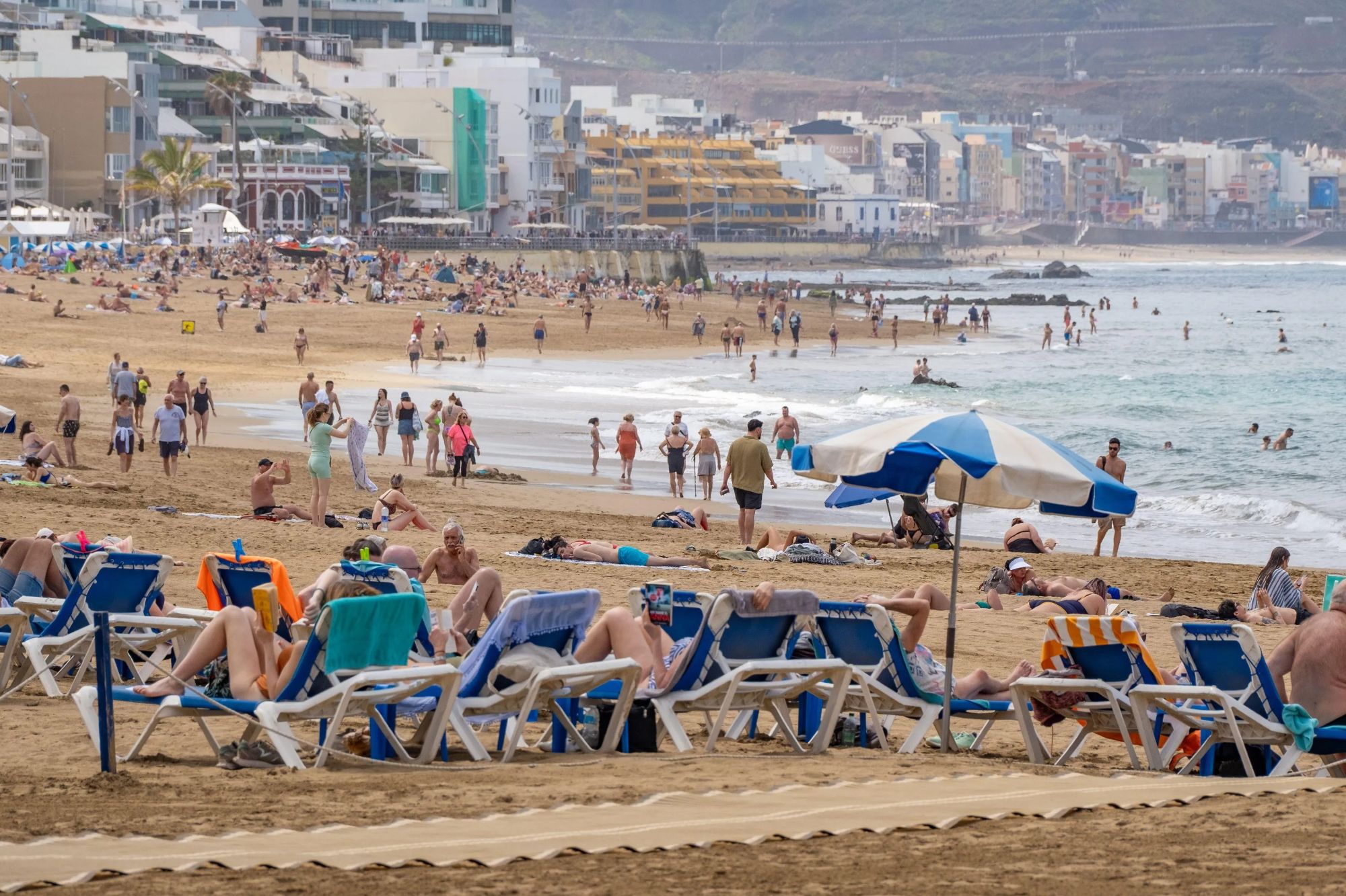An image collage containing 1 images, Image 1 shows Tourists on the city beach in Las Palmas, Gran Canaria, enjoying a sunny day after torrential rain