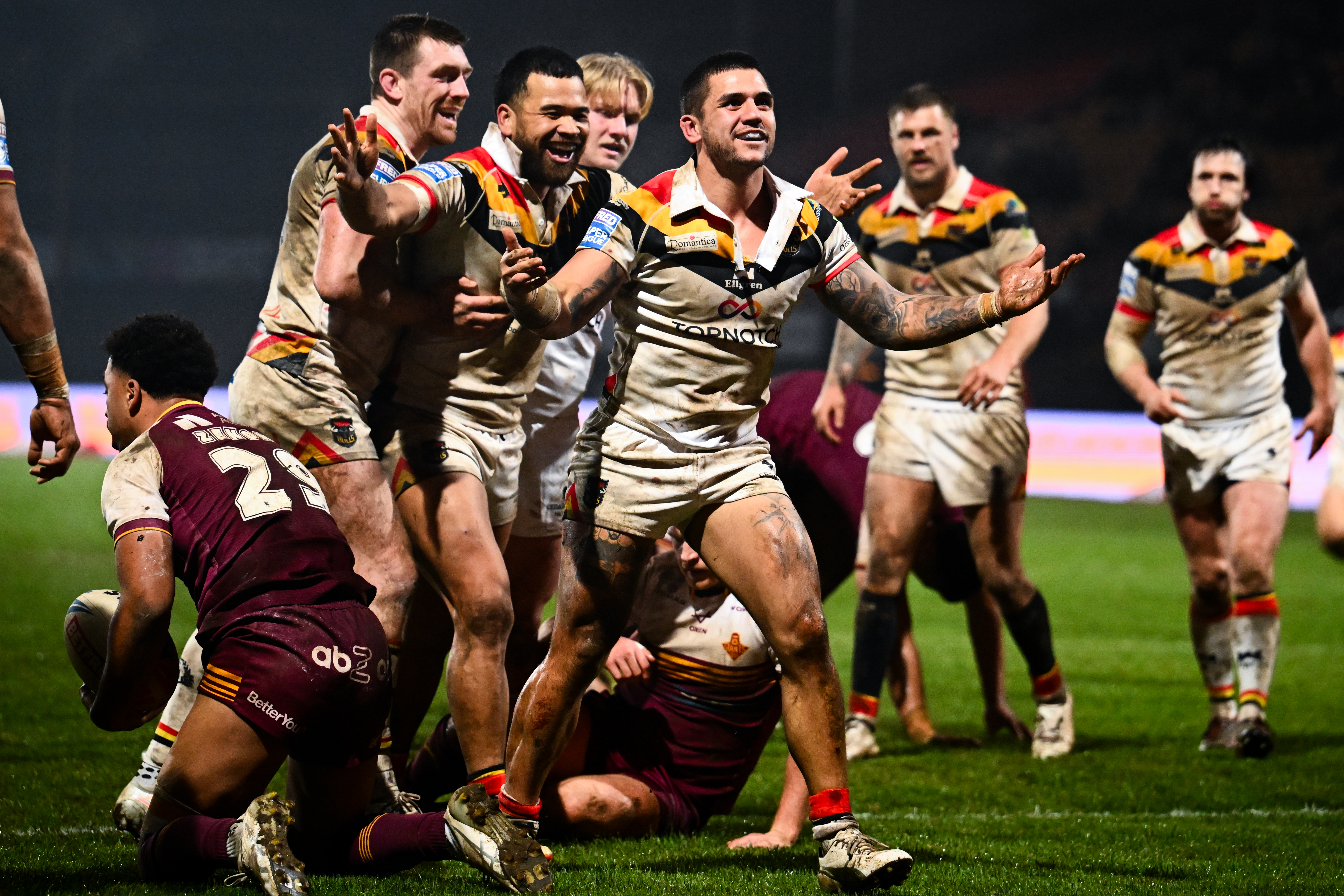 Bradford Bulls players celebrate a try against Huddersfield Giants, while a Giants player kneels in the foreground.