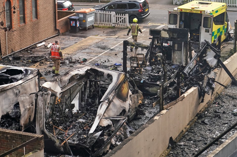 View of burnt ambulances in a car park with firefighters investigating.