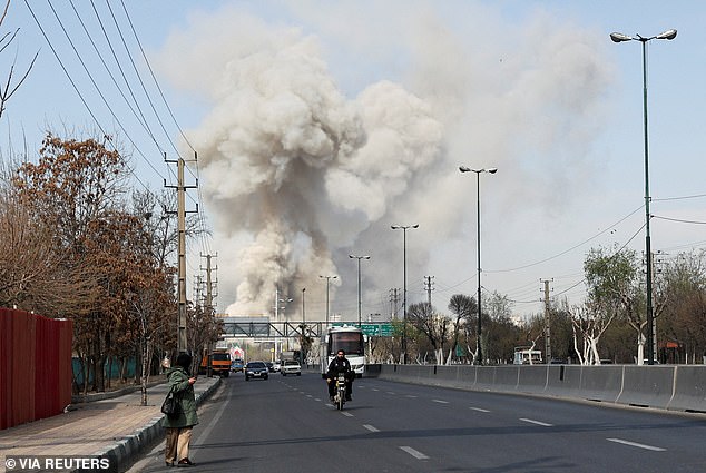 People gather on the sides of a road as smoke rises in the background following an explosion in Tehran yesterday