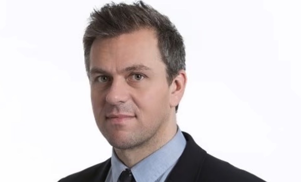Headshot of a man with short, dark hair, blue collared shirt, and a dark suit jacket.