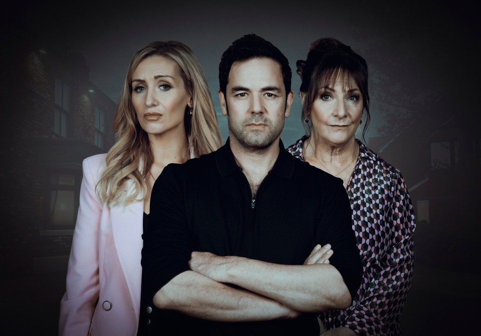 Three people, two women and a man, standing in front of a dark, blurred background of houses.