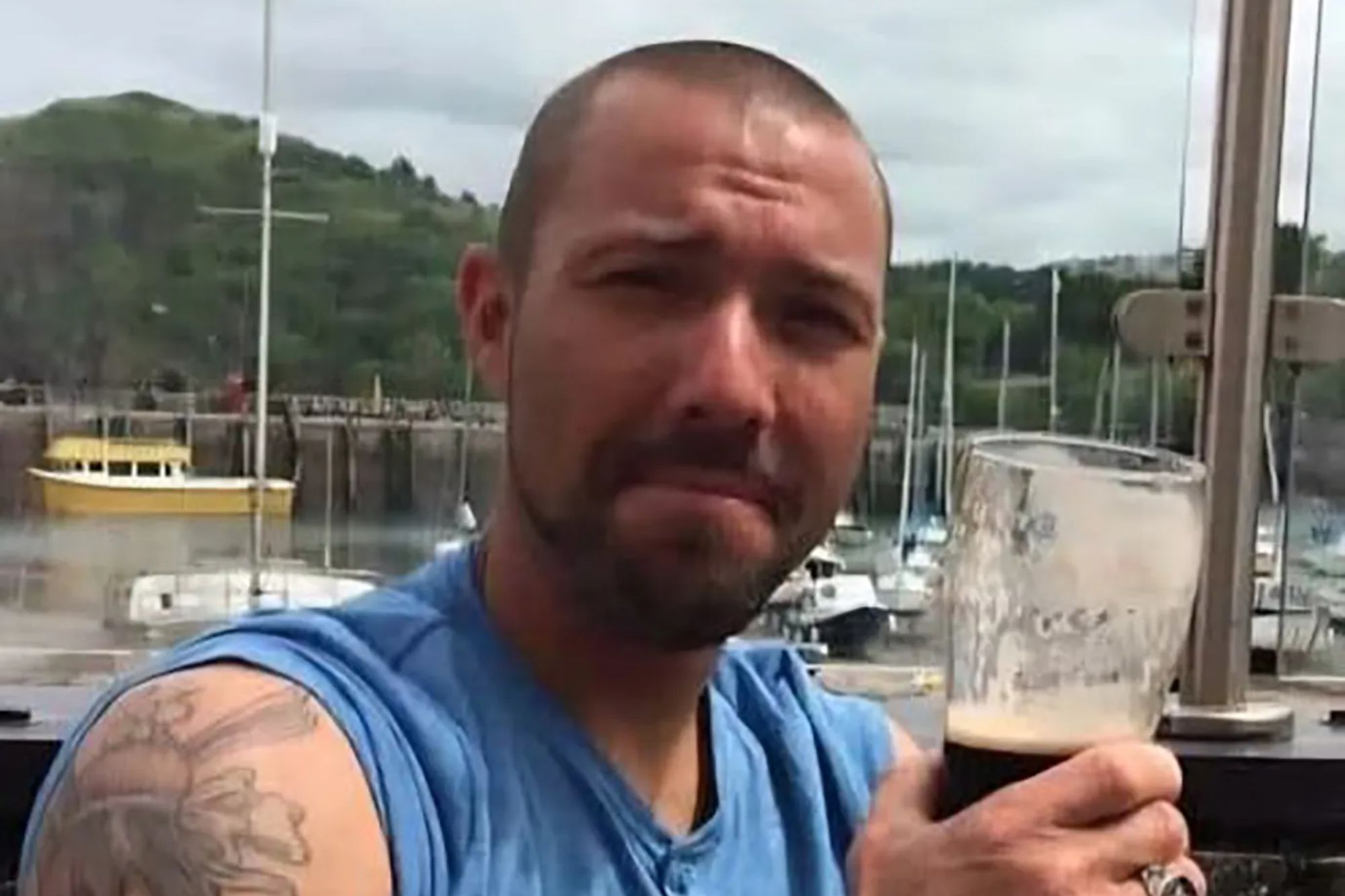 An image collage containing 1 images, Image 1 shows Andrew Freakley holding a pint of Guinness with a harbor and boats in the background