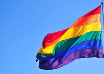 A rainbow "pride" flag waves in front of a blue sky.