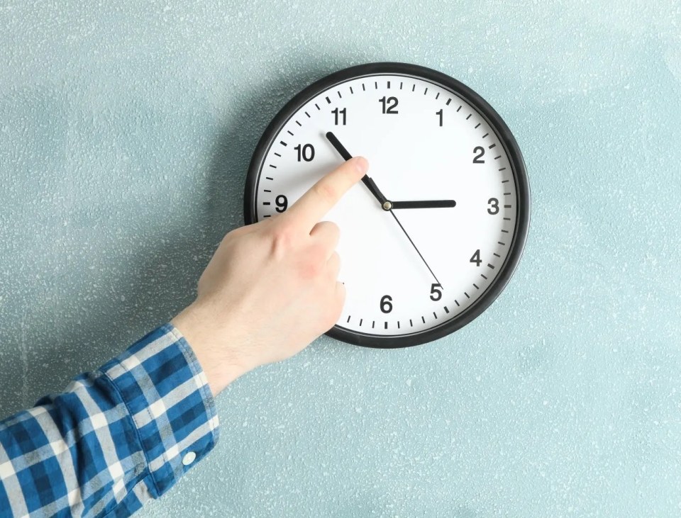 A hand adjusting the hands of a wall clock, set to approximately 10:15.