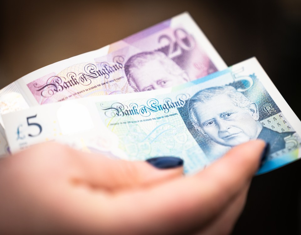 A woman's hand holding a £20 and a £5 British banknote.