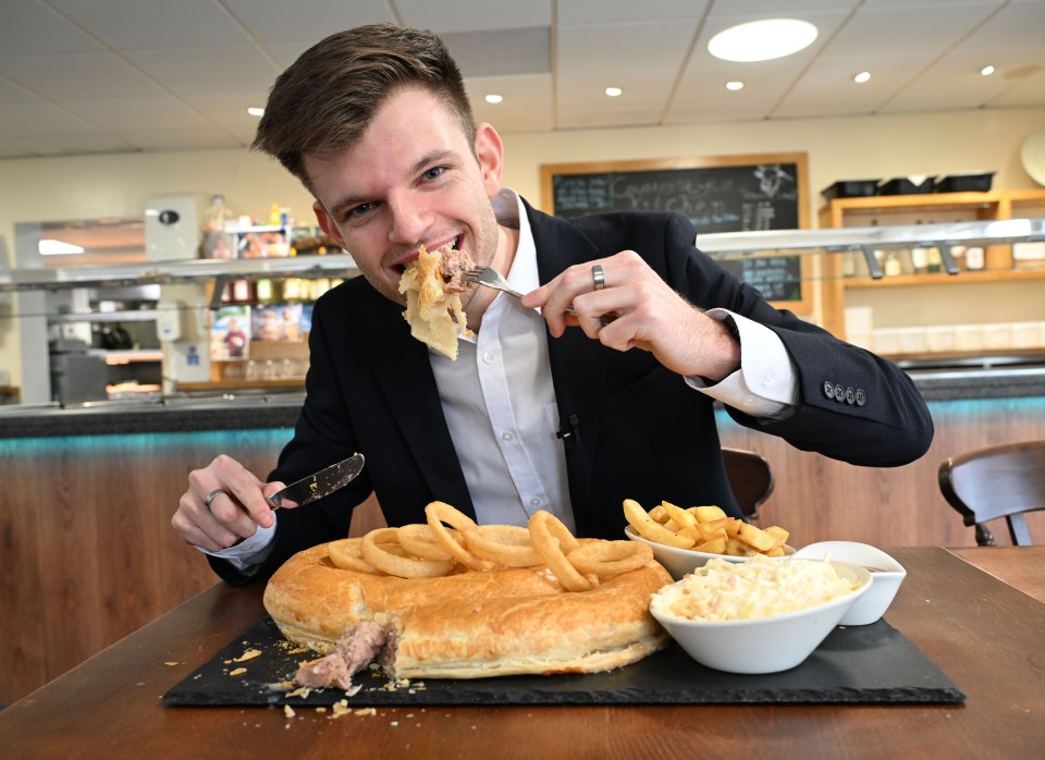 A man attempting to eat a 4ft sausage roll with onion rings, chips, and coleslaw.