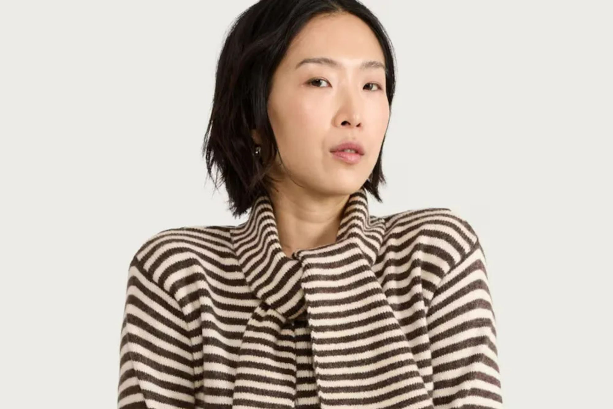 An image collage containing 1 images, Image 1 shows A woman models a brown and white striped cardigan with an integrated scarf and light wash jeans