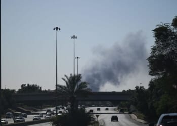 Motorists drive along a street as smoke rises from a reported Iranian strike in the area where the U.S. Embassy is located in Kuwait City on March 2, 2026.