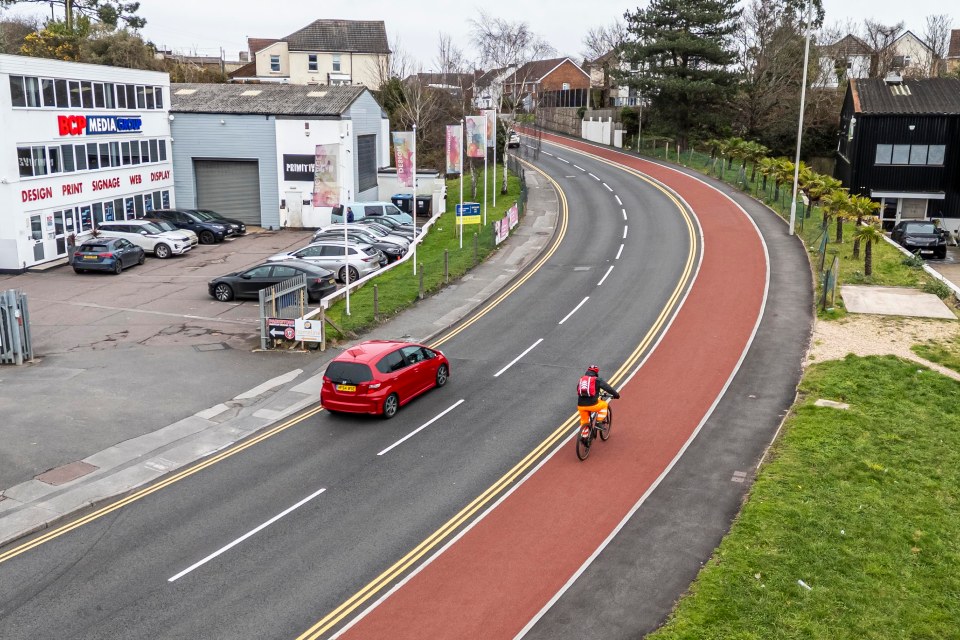 Cyclist on a red bike lane next to a road with a red car.