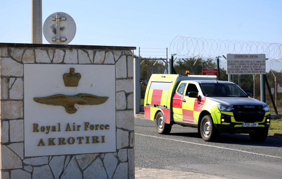 A yellow and red truck leaves the entrance of RAF Akrotiri, marked with a sign.