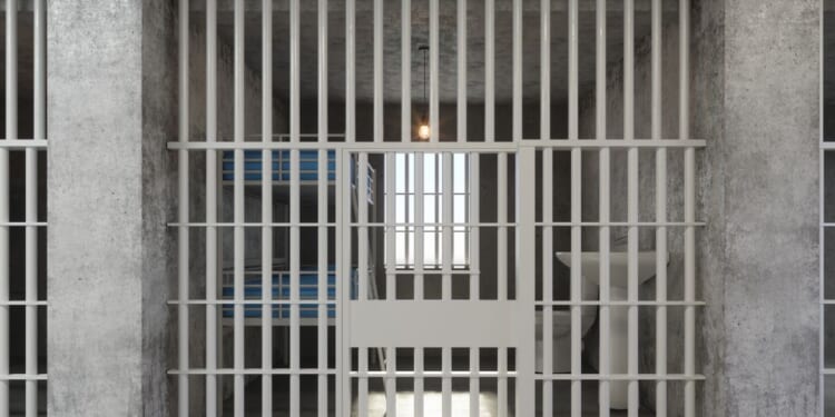 The front view of an empty prison cell with a bunkbed and sink.