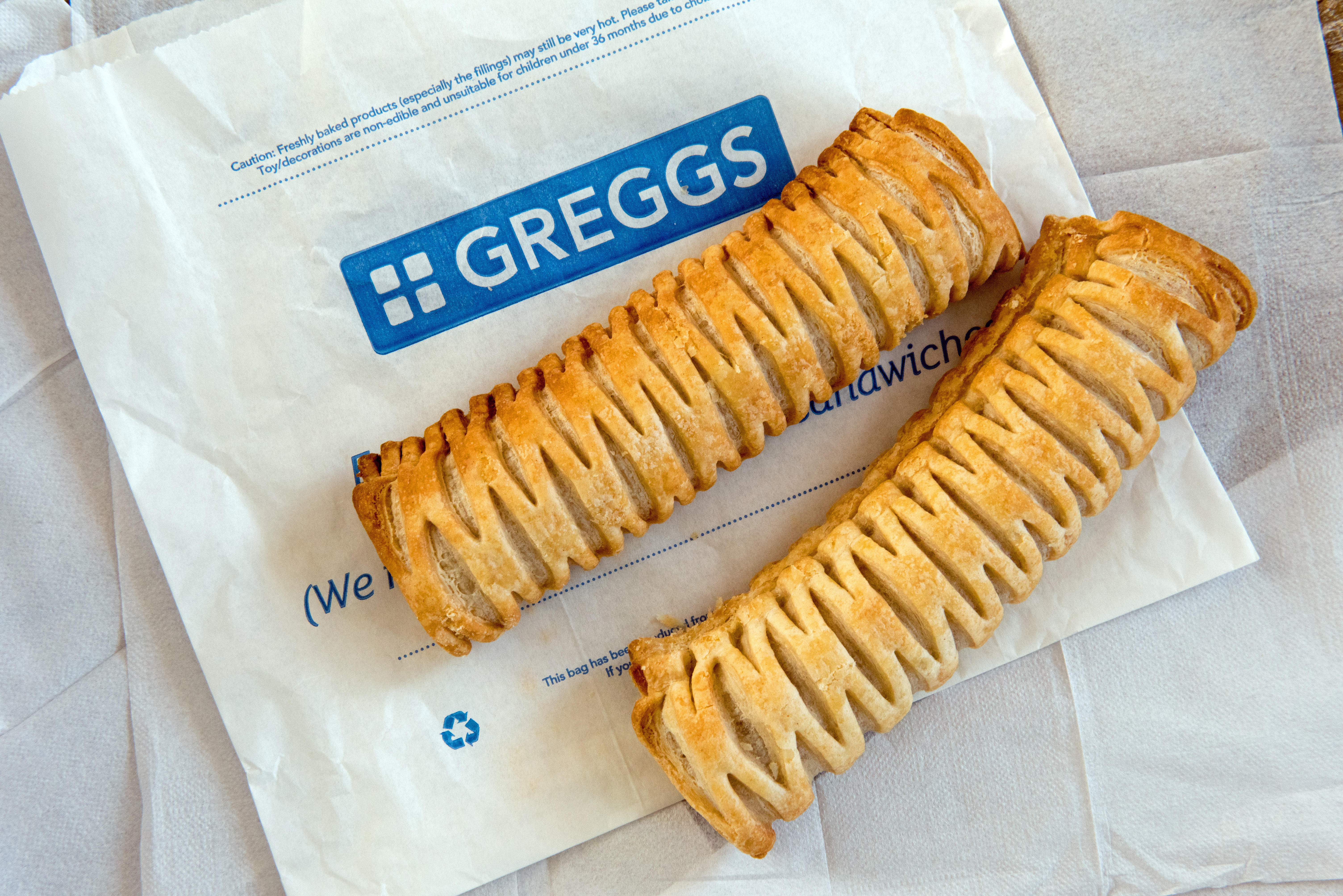 Two Greggs Vegan Sausage Rolls on paper bag with paper napkins behind.