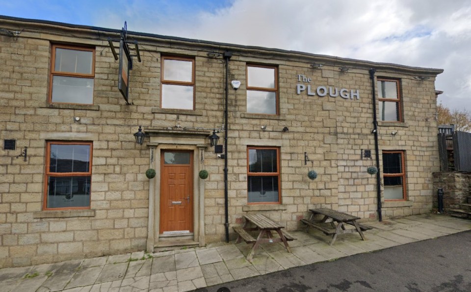 Exterior of The Plough pub, a stone building with "The Plough" sign on its facade, and two picnic tables outside.