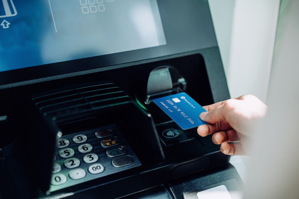 A hand inserting a blue bank card into an ATM.