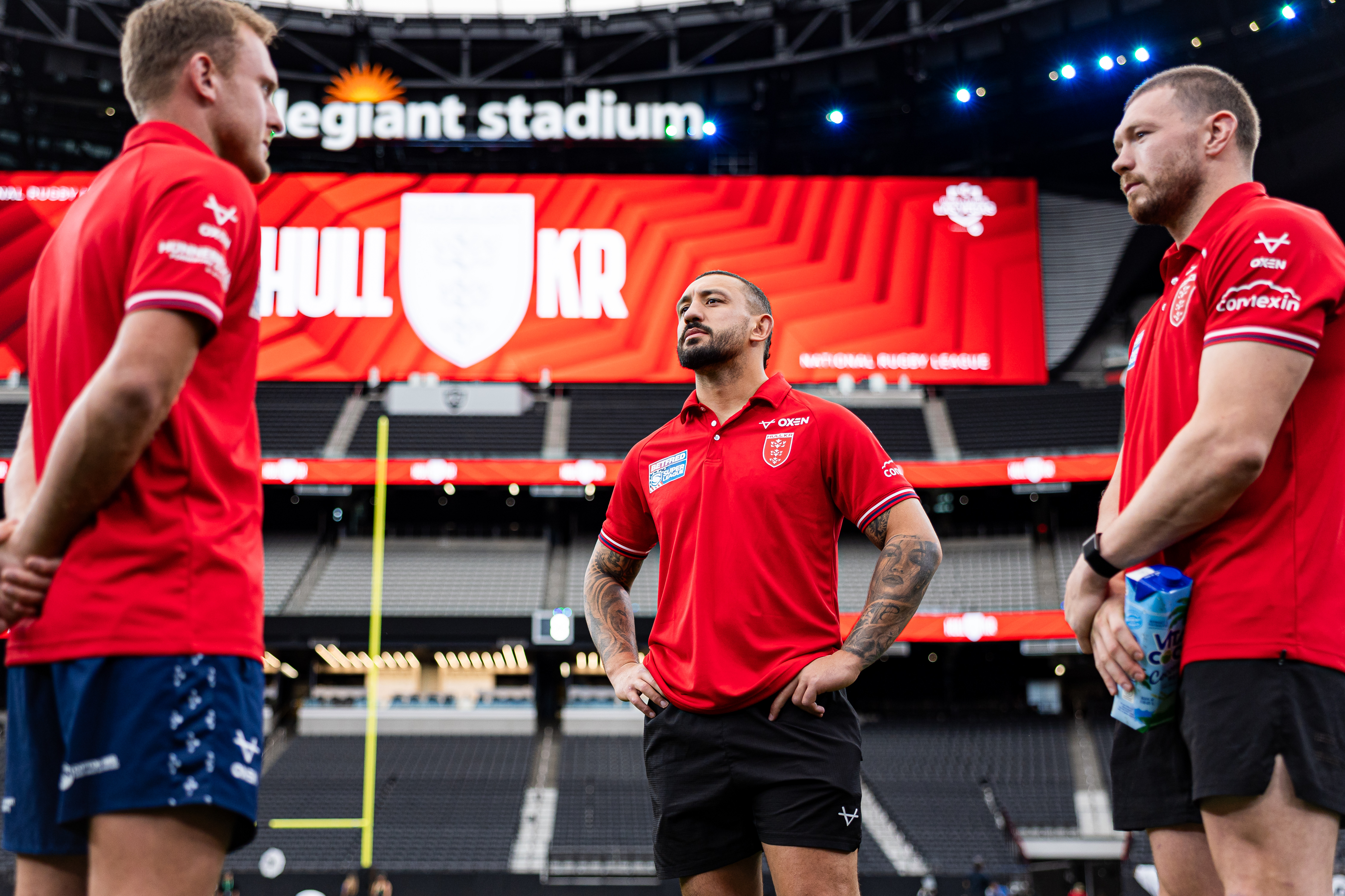 Three rugby players in red shirts on the field during a captain's run at Allegiant Stadium.
