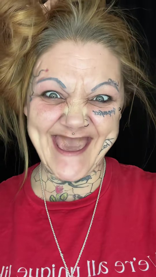 A woman in a red shirt with exaggerated, distorted facial features, wide eyes, and tattoos on her face and neck.