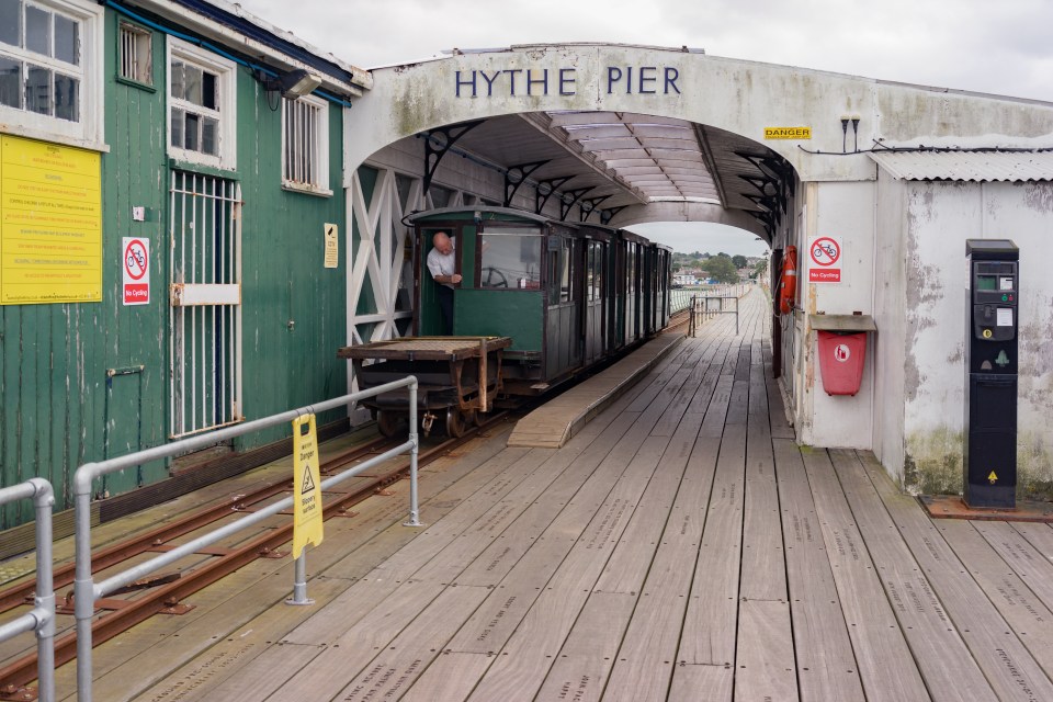 A man leaning out of the Hythe Pier railway car on the wooden pier.