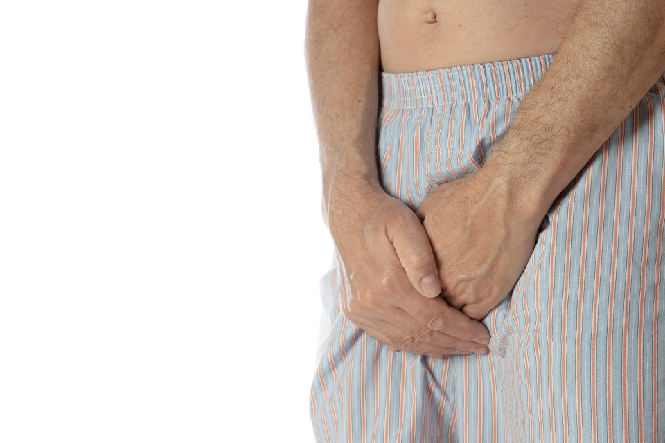 A man in blue and orange striped boxer shorts holds his hands over his groin area.
