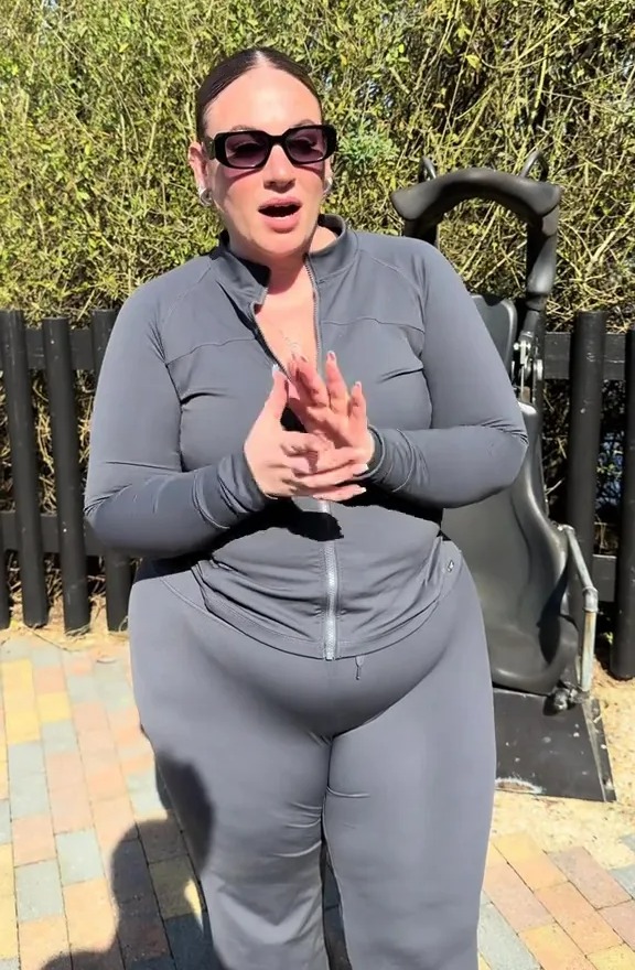 Woman in grey athleisure wear and sunglasses speaking outdoors.