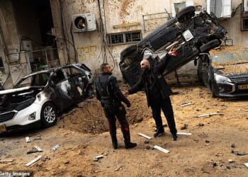 First responders stand near a crater and damaged cars in Holon, Israel after a strike today