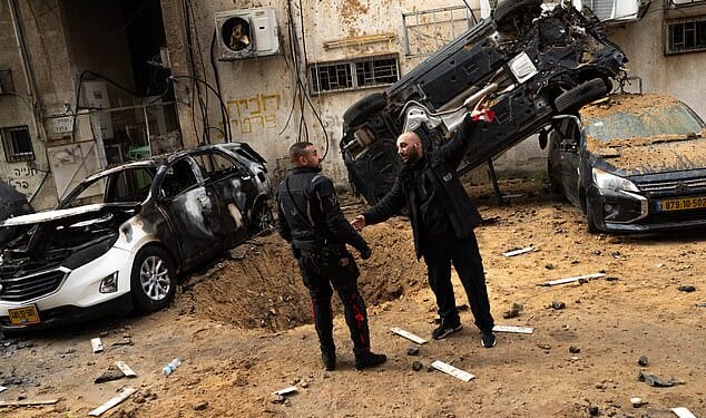 First responders stand near a crater and damaged cars in Holon, Israel after a strike today