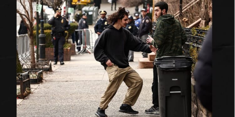 A left-wing activist is handed a homemade explosive device by a fellow activist before throwing it toward police during an anti-Islamic protest Saturday in front of Gracie Mansion, New York mayor Zohran Mamdani's official residence.