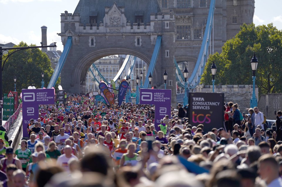 Crowd of runners participating in the TCS London Marathon, passing by the Tower Bridge.