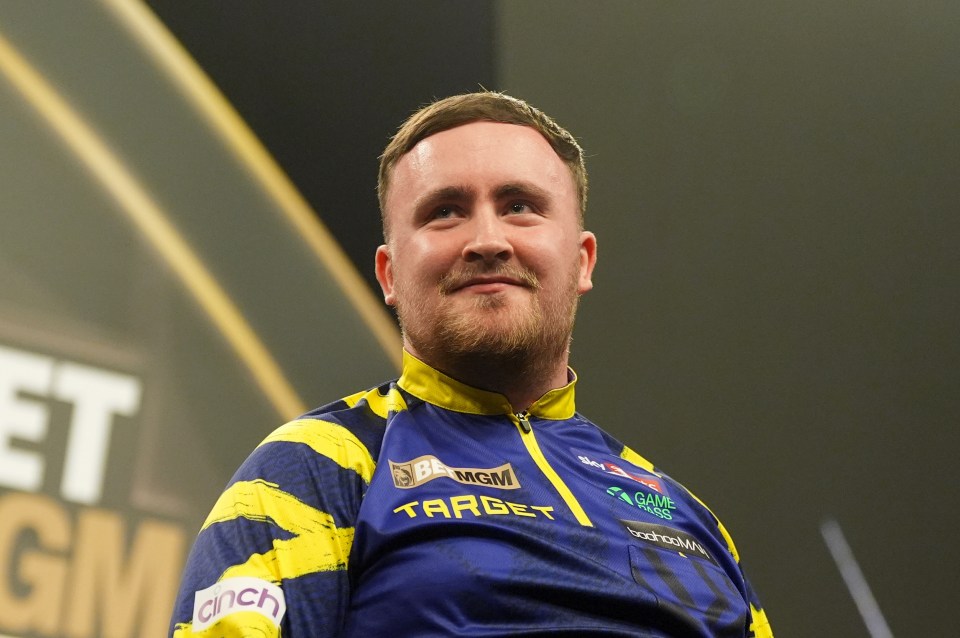 Luke Littler in a blue and yellow shirt smiling.