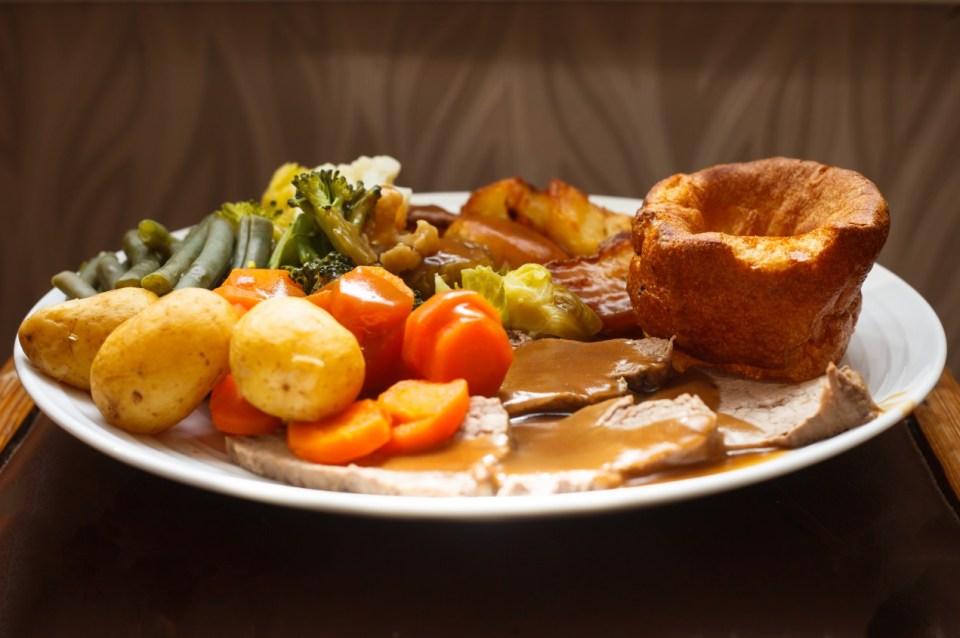 Roast beef dinner with Yorkshire pudding, gravy, potatoes, carrots, green beans, and broccoli.